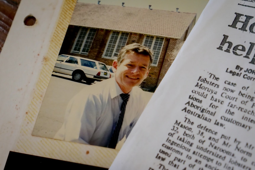 Photo of man in his 40s in a shirt and tie in an album with a portion of a news clipping lying on top.