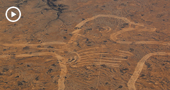 Wide aerial shot of a enormous figure drawn in brown desert sand.