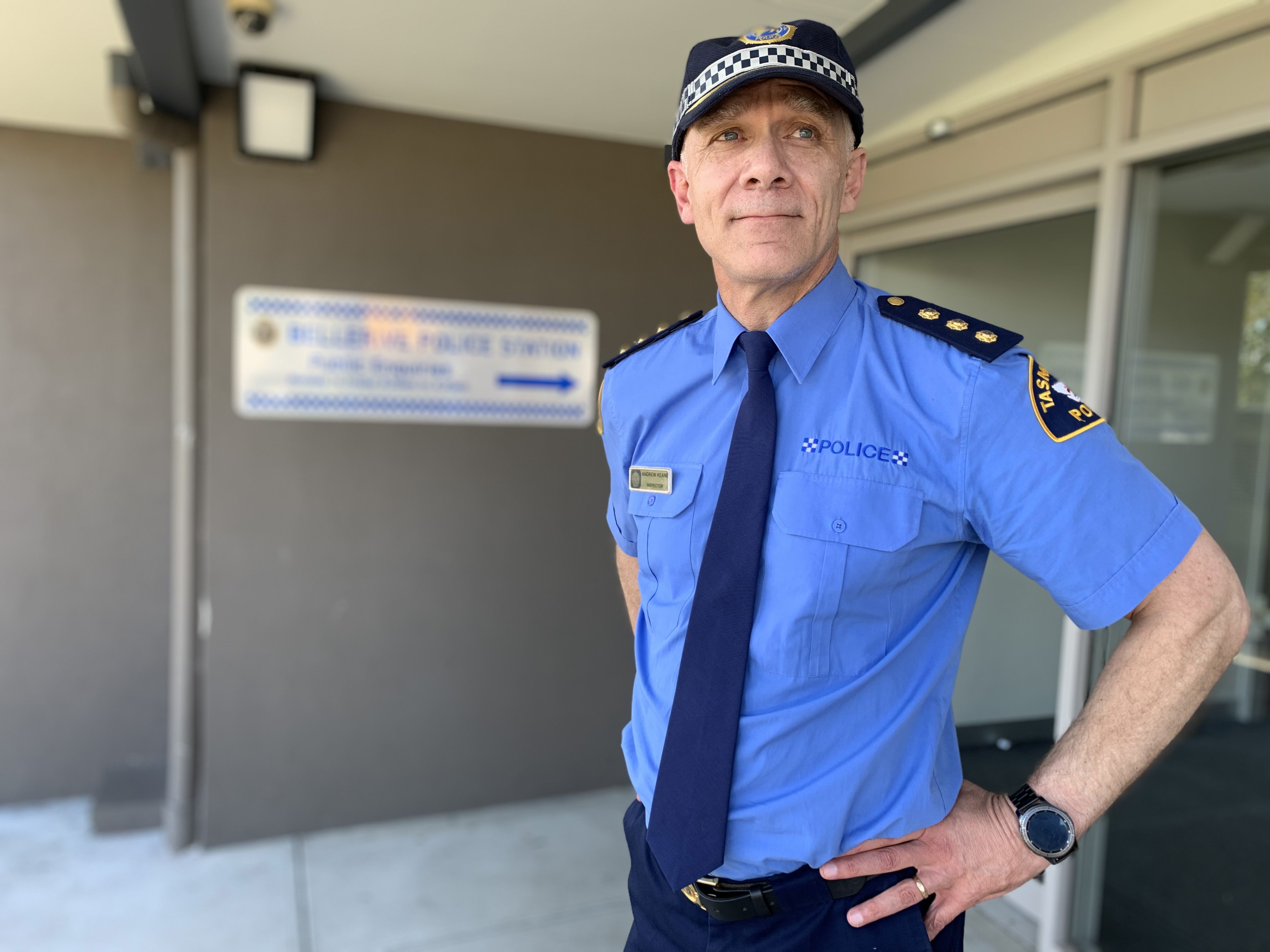 A police officer stands with his hands on his hips outside a police station.