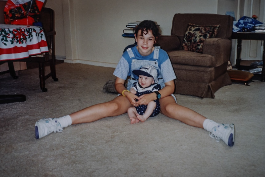 a young Angela in her early teens sits with baby bridget in between her legs in a living room