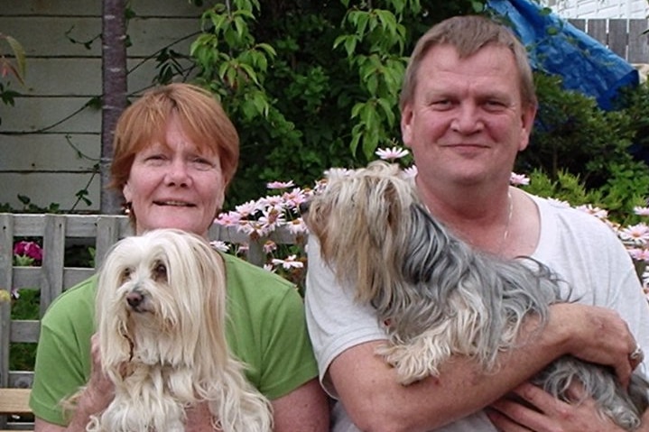 A woman and man sit together, each holding a small dog in their arms.