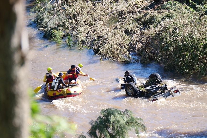 Diver and emergency services search an upturned car at flooded Canungra Creek.