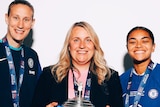 Chelsea WSL manager Emma Hayes holds the FA Cup while standing between players Ann-Katrin Berger and Jess Carter.