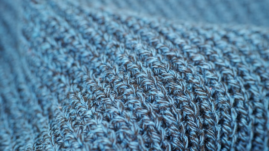 Close up of a cerulean blue knitted item of clothing. The yarn is soft and has flecks of black in it.