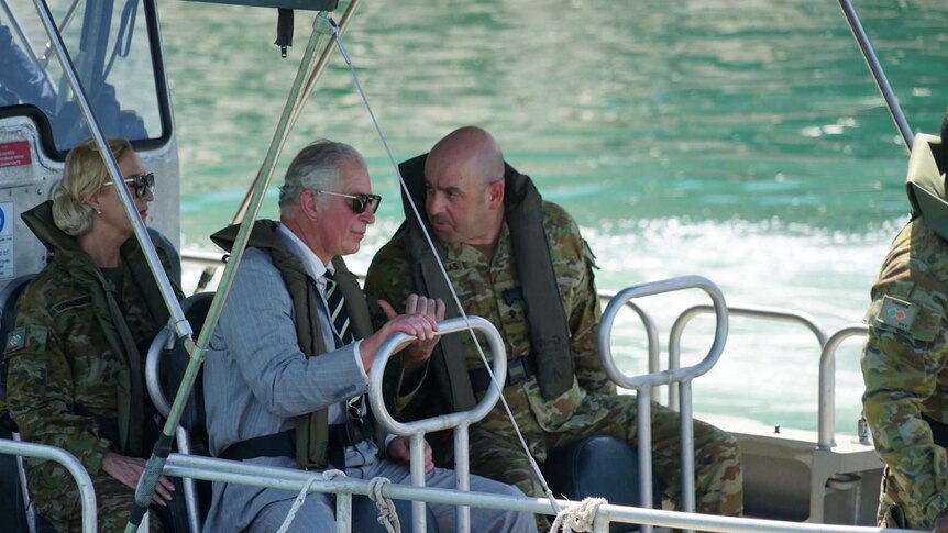 Prince Charles wears a lifejacket and speaks with a Commander as he crosses the harbour in a boat