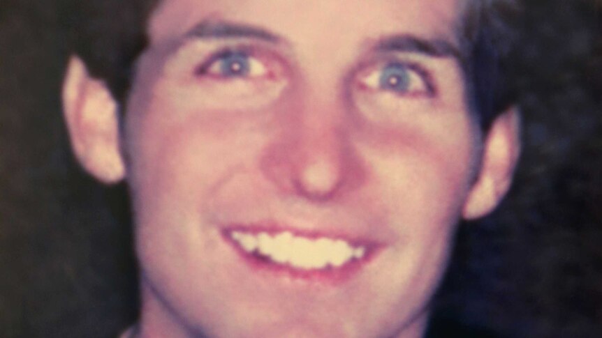 A photo of a blue-eyed young man with dark hair smiling at the camera.