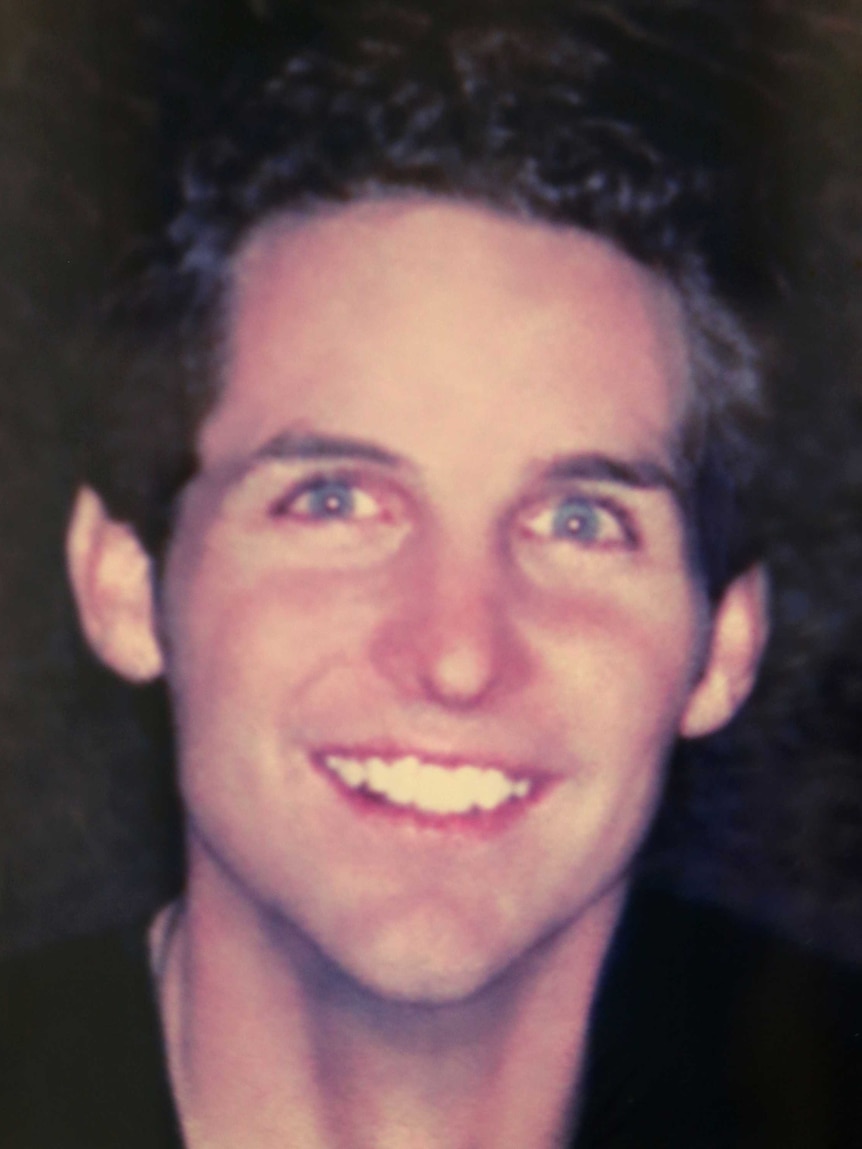 A photo of a blue-eyed young man with dark hair smiling at the camera.