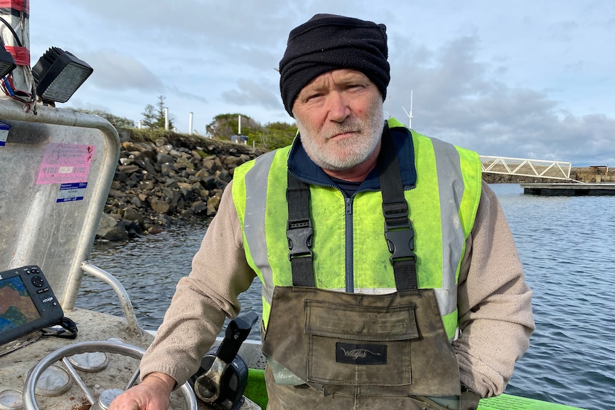 A bearded man in a fishing vest sits in a boat
