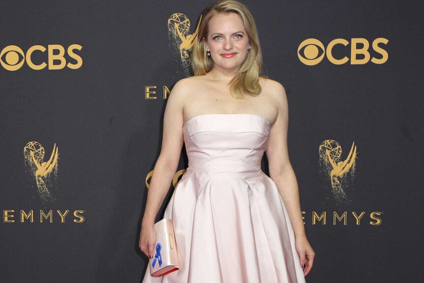 Actress Elisabeth Moss is wearing a light pink dress and matching clutch that has a blue pin on it.