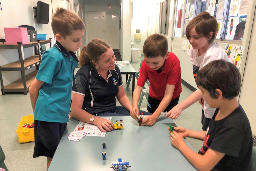 A woman sitting at a table talking to a group of young boys.