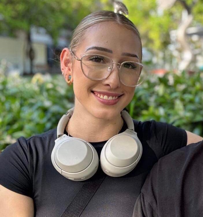 a girl with glasses, black top smiles with headphones around her neck. 