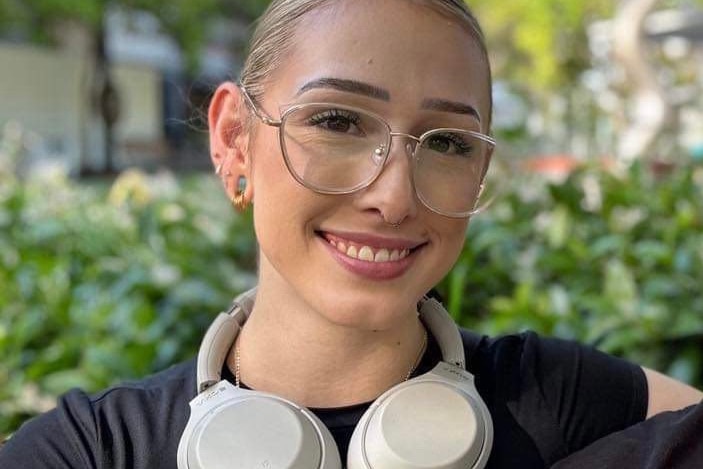 a girl with glasses, black top smiles with headphones around her neck. 