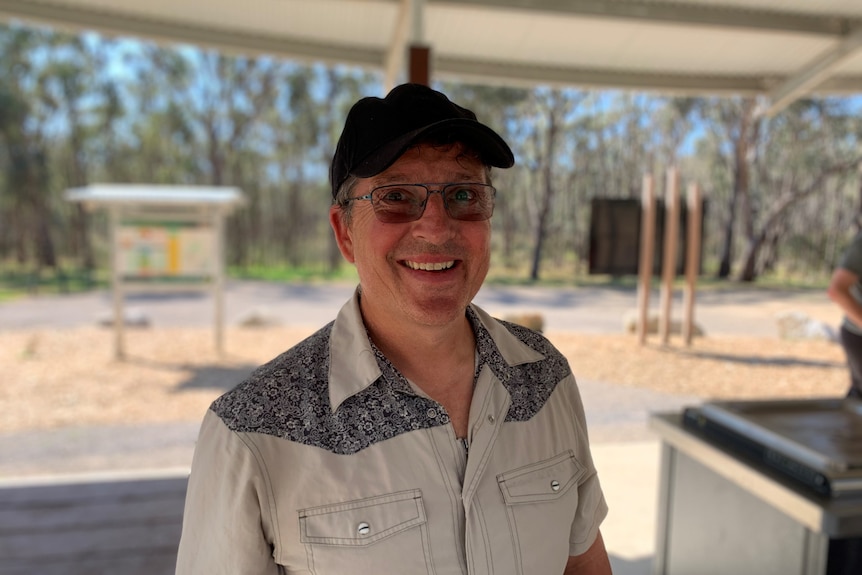 Man wearing glasses and a cap standing in a park picnic area.