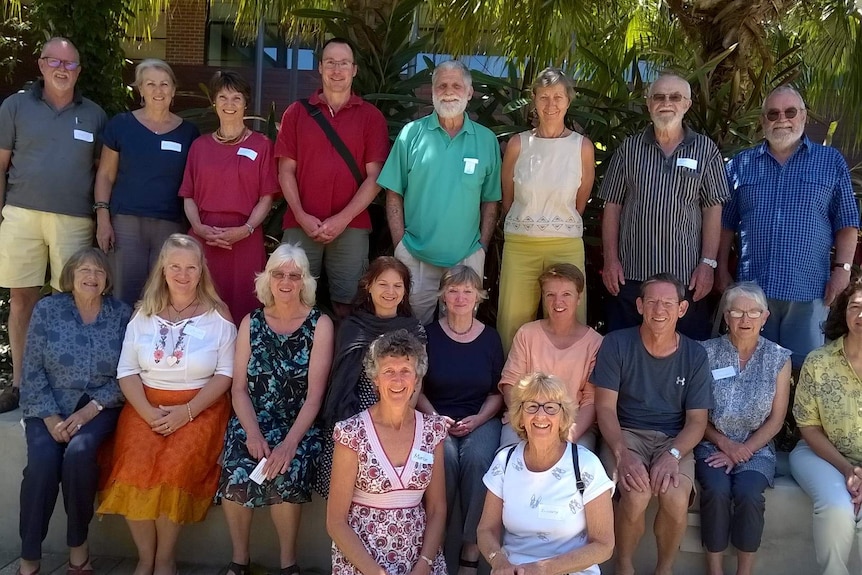 About 20 people, mainly of retiree-age, wearing name tags, smile together for a group photo outdoors.