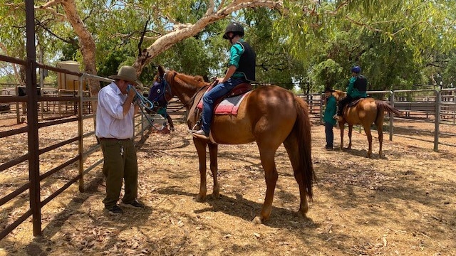 boy on horse in a yard with a teacher standing nearby 