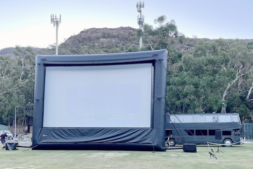 A large inflatable outdoor movie screen in a grassy park 