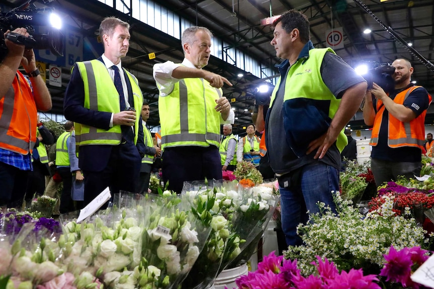 the Labor leader talks with a flower stallholder surrounded by flowers and press