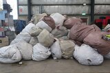 Piles of large bags full of textiles sit in a warehouse.