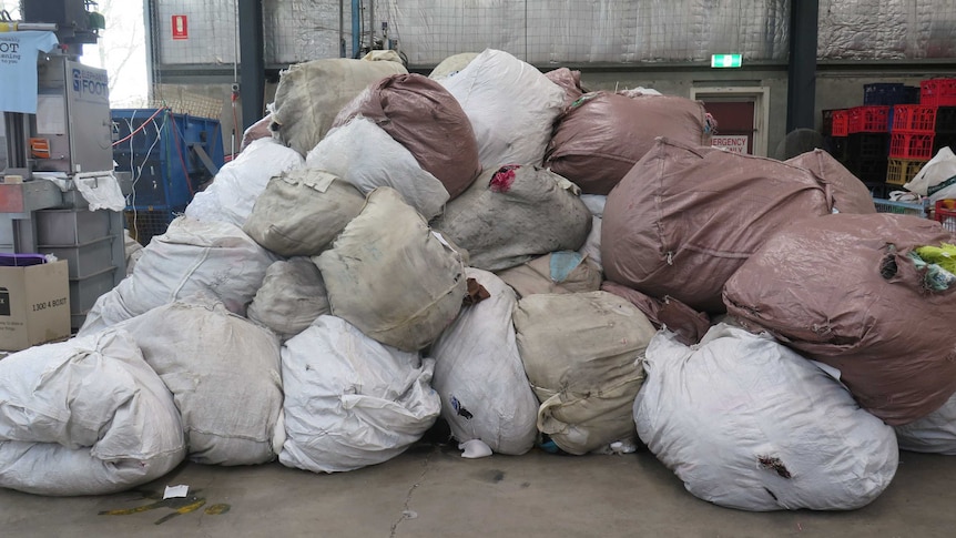 Piles of large bags full of textiles sit in a warehouse.