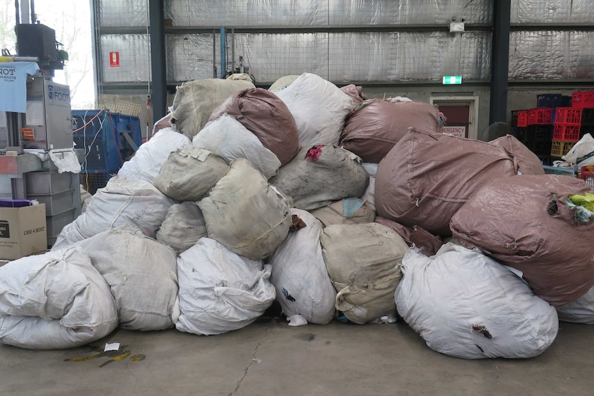 Piles of large bags full of textiles sit in a warehouse.