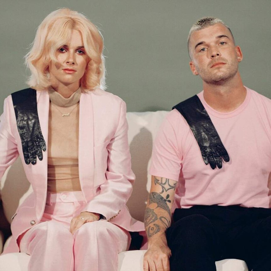 Broods dressed in pastel pink, sitting on a couch