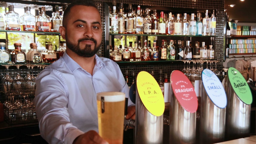 Royal On The Waterfront manager Anoop Nair poses for a photo behind a bar holding a pint of beer on the counter.