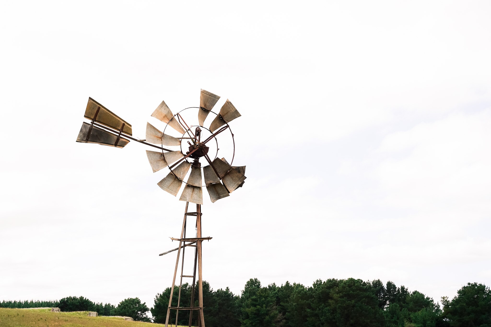 An old rusty windmill in a paddock on an overcast day.