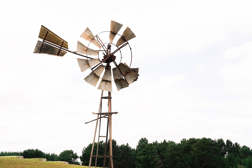 An old rusty windmill in a paddock on an overcast day.