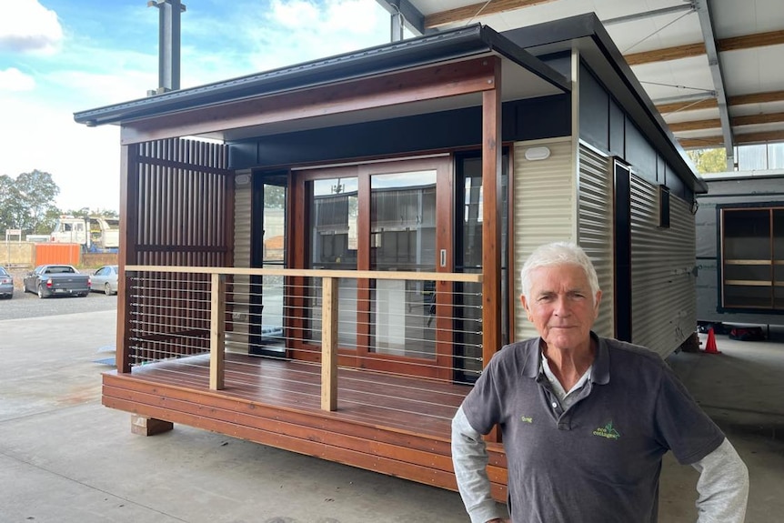 An older man standing in front of a small house.