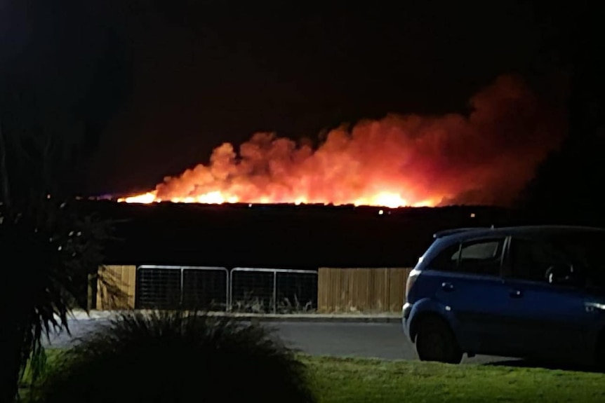 A large bushfire and smoke burns on a beachside spit of land.