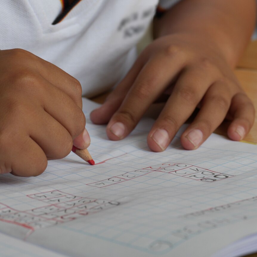 A child's hands write on grid paper with a simple equation written on it.