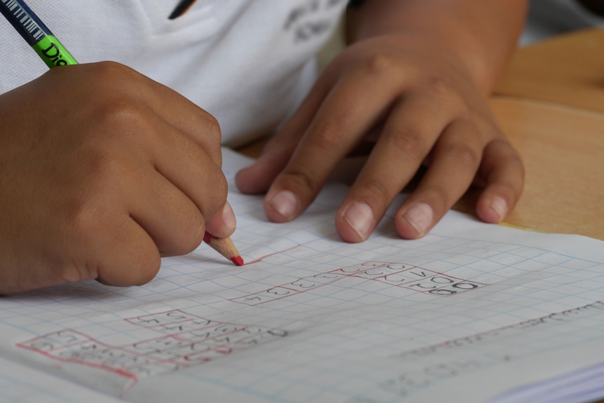 A child's hands write on grid paper with a simple equation written on it.