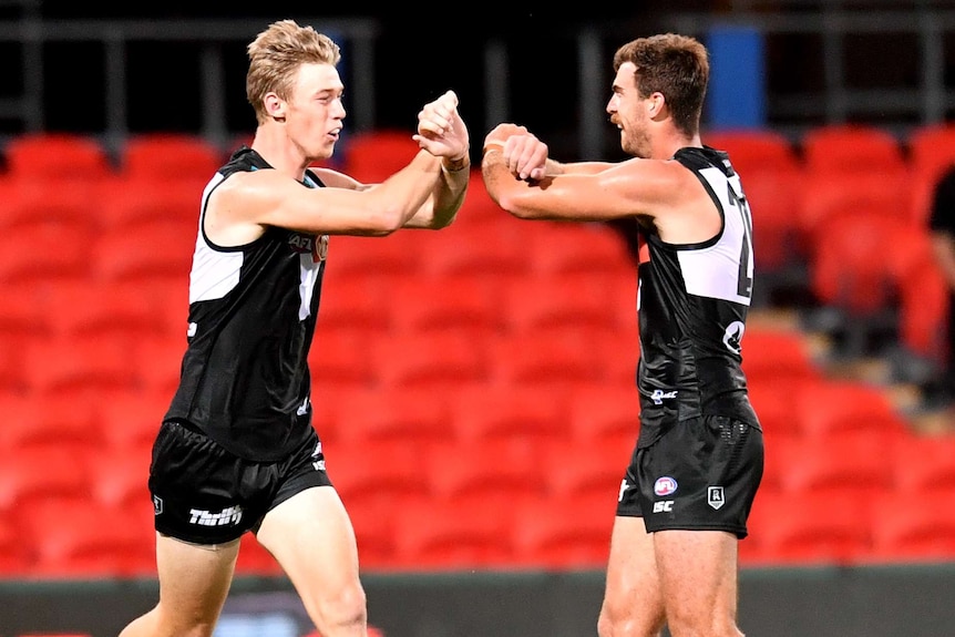 Two Port Adelaide AFL players celebrate with an elbow bump in response to coronavirus precautionary measures.