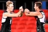 Two Port Adelaide AFL players celebrate with an elbow bump in response to coronavirus precautionary measures.