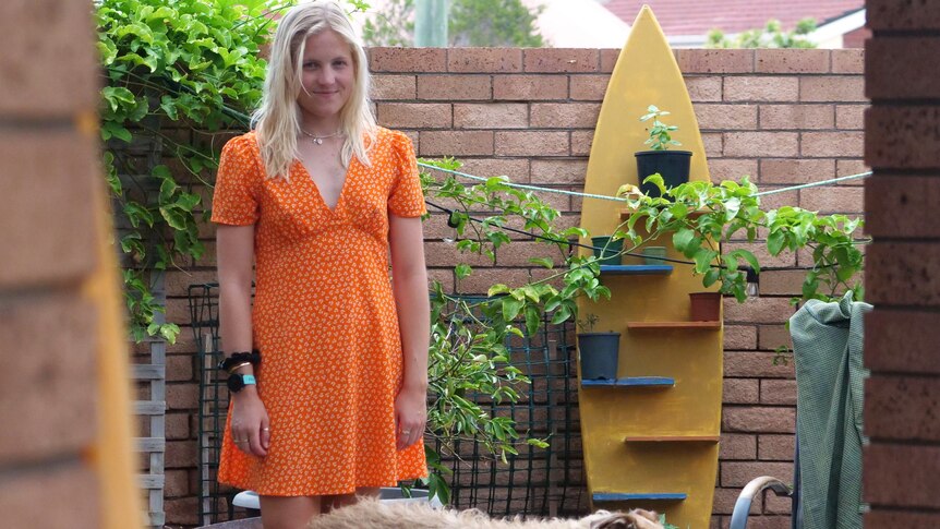 Woman with blonde hair and orange dog stands in garden area with dog. 