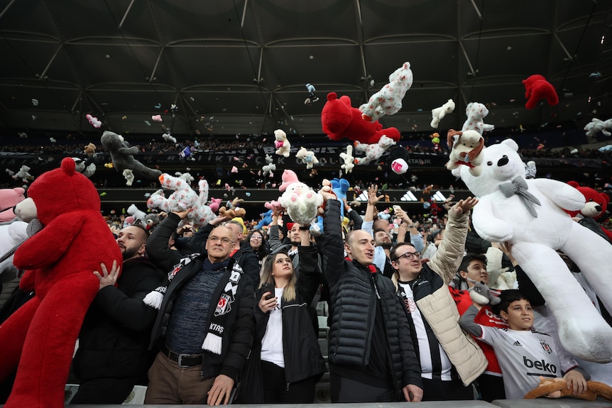 Football fans inside a stadium throwing stuffed toys onto the pitch