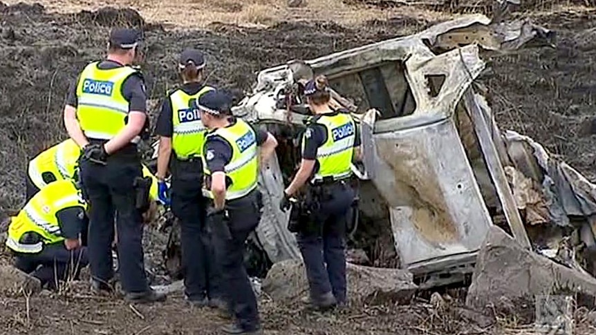 Police stand next to the burnt remains of the ute, with charred earth all around them.