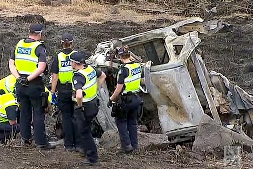 Police stand next to the burnt remains of the ute, with charred earth all around them.