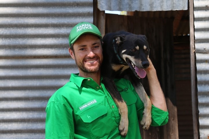 Jack wears a green hat and shirt with 'Farms Advice' on both. He smiles in front of a shed holding his dog.