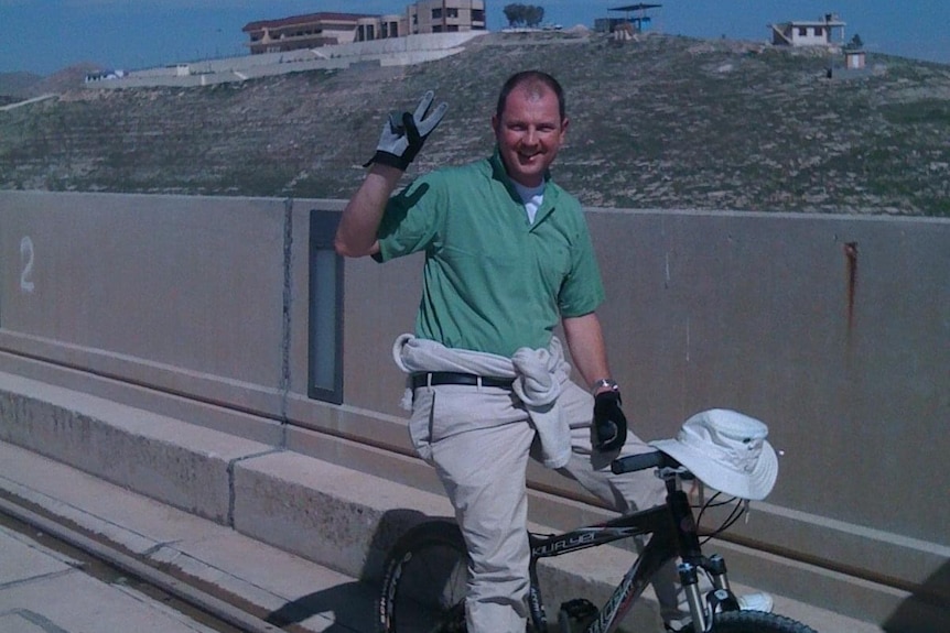 A man on a bike giving the peace sign.