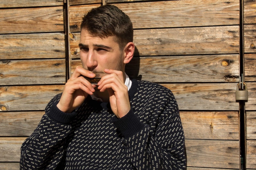Solomon Frank playing harmonica in front of wood background