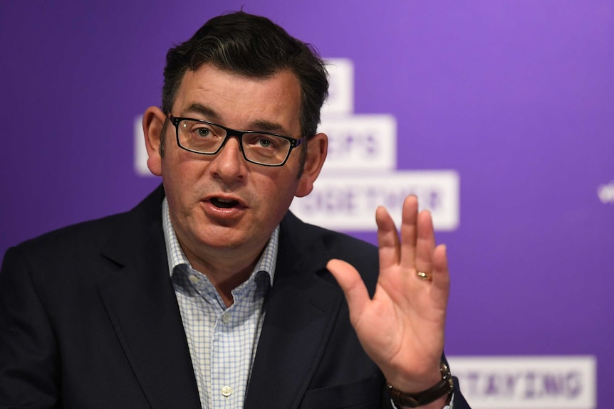 Daniel Andrews holds up his left hand while talking at a press conference.