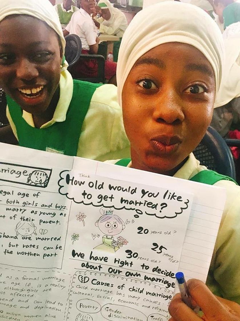 Two girls in an African classroom hold up an exercise book with words and pictures in it.
