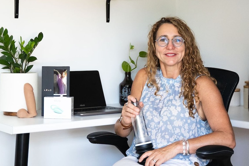 A woman sits at a desk with a penis pump. 