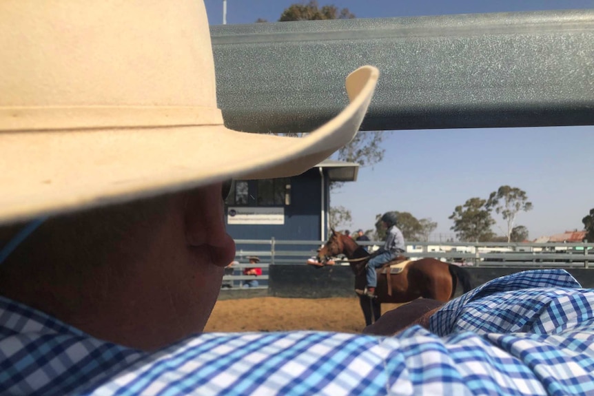 A man peers through rails watching his son get ready to ride campdraft