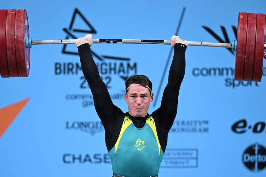 A man wearing green, yellow and black lifts a heavy weight during a competition