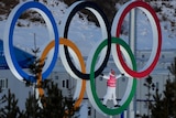 A person stands inside the Olympic Rings in front of a snow covered slope