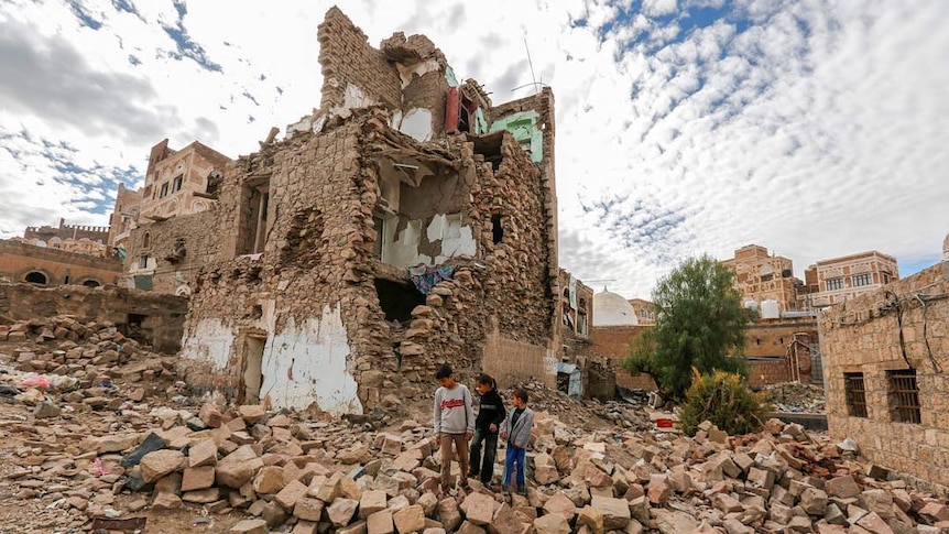 Three boys walk among the rubble of a bombed building in Sana'a, Yemen