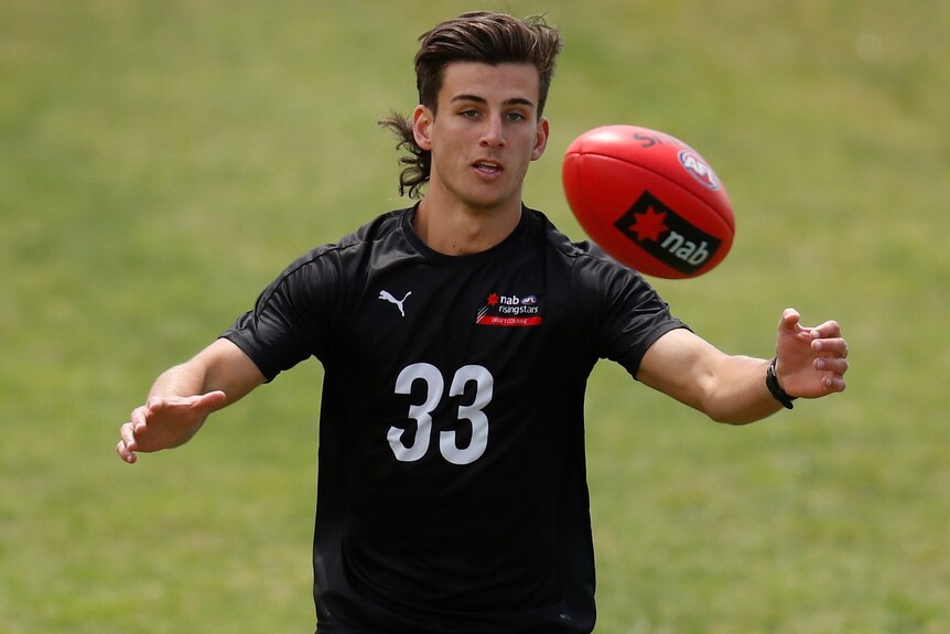 A prospective AFL player looks to catch the ball during a training session.