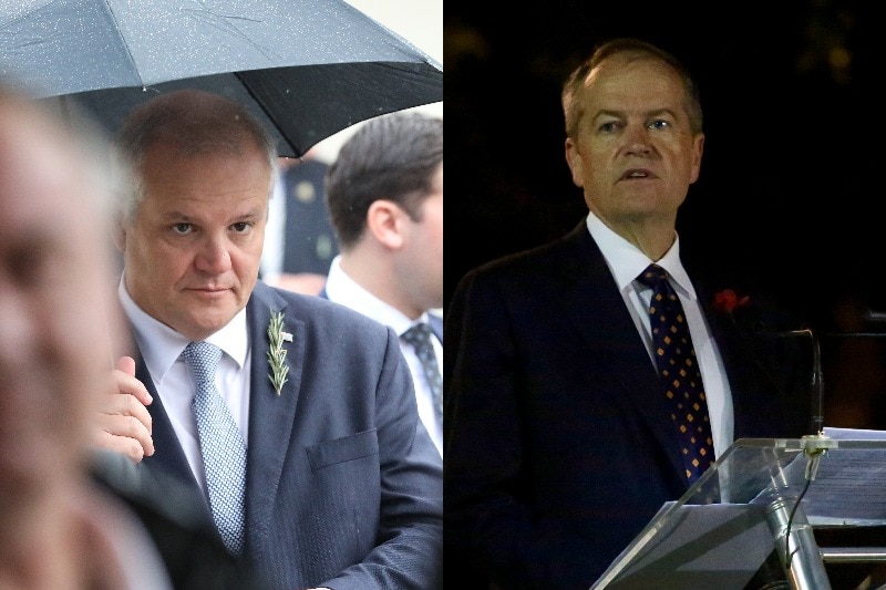 A man stands at a dark podium to speak, and another man walks through the rain with an umbrella.